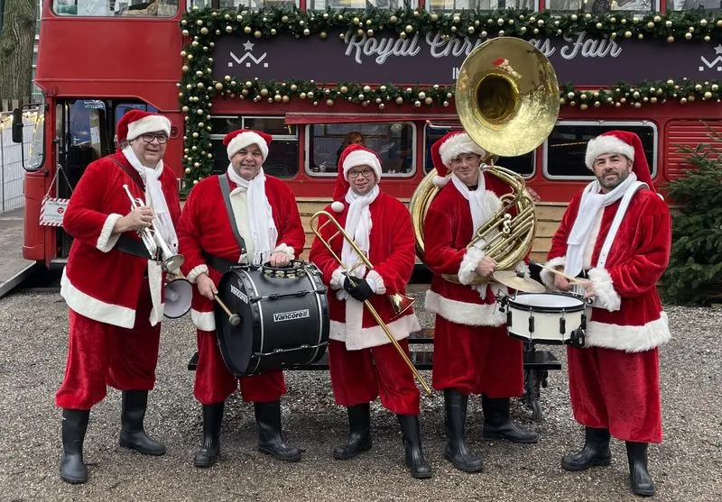Dixielandband in kerstpakken met trompet, trommels en sousafoon voor een rode dubbeldekkerbus